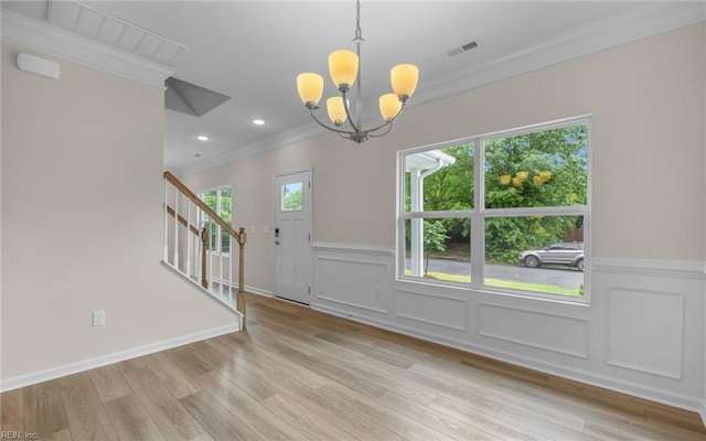 entrance foyer with crown molding, stairs, a chandelier, a wainscoted wall, and light wood-type flooring