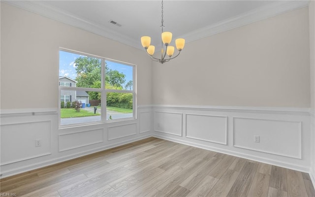 unfurnished dining area with a chandelier, crown molding, wainscoting, light wood-style flooring, and a decorative wall