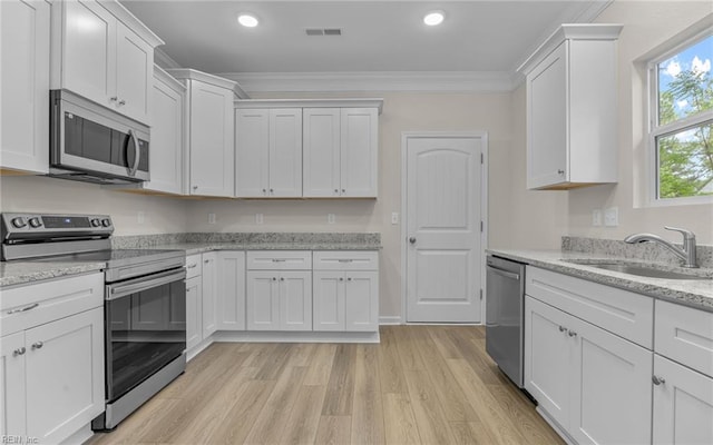 kitchen with appliances with stainless steel finishes, a sink, white cabinetry, crown molding, and light wood-style flooring