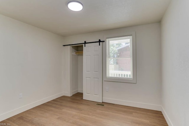 1413 Elm Ave, Portsmouth, VA 23704 - unfurnished bedroom featuring a barn door, baseboards, light wood-style flooring, and a closet