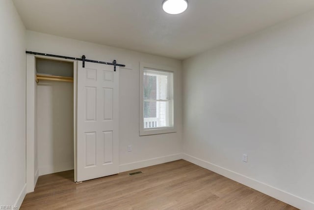 1413 Elm Ave, Portsmouth, VA 23704 - unfurnished bedroom with light wood-type flooring, baseboards, and a barn door