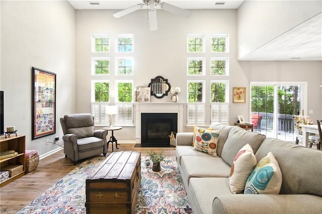 living room with a high ceiling, wood finished floors, plenty of natural light, a ceiling fan, and a fireplace with flush hearth