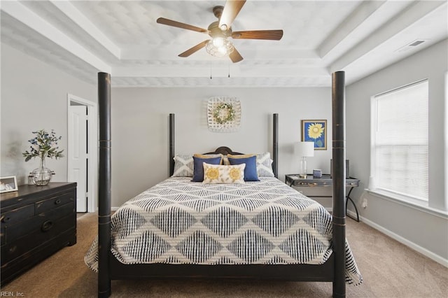 carpeted bedroom with a raised ceiling, multiple windows, and baseboards