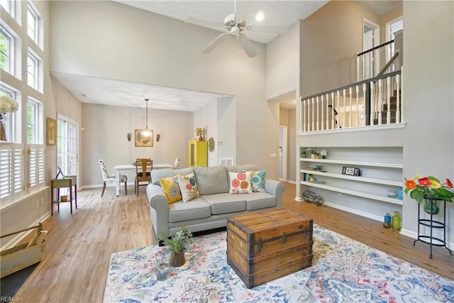 living area with a towering ceiling, wood finished floors, a ceiling fan, plenty of natural light, and built in features