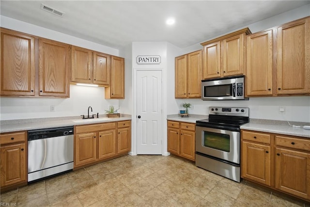kitchen featuring appliances with stainless steel finishes, a sink, light countertops, and brown cabinetry