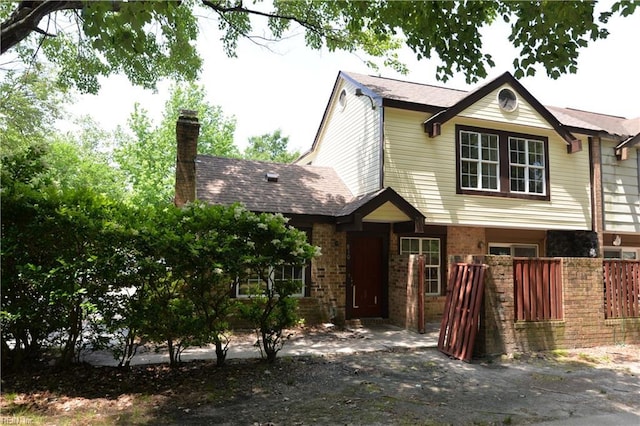 view of front of house featuring brick siding, a chimney, and fence