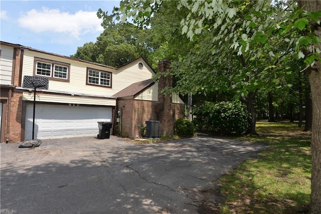 view of front of home featuring driveway, a garage, a chimney, brick siding, and cooling unit