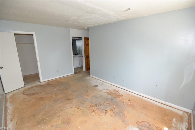 unfurnished bedroom with a walk in closet, baseboards, a closet, and connected bathroom