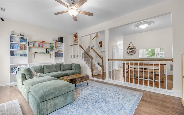 living area featuring wood finished floors, ceiling fan, stairs, and baseboards