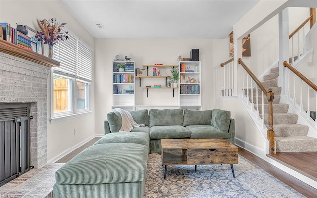 living area featuring wood finished floors, baseboards, stairs, and a brick fireplace