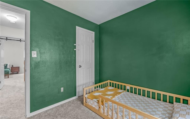 bedroom with carpet floors, a barn door, and baseboards