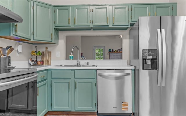 kitchen with stainless steel appliances, a sink, light countertops, under cabinet range hood, and green cabinets