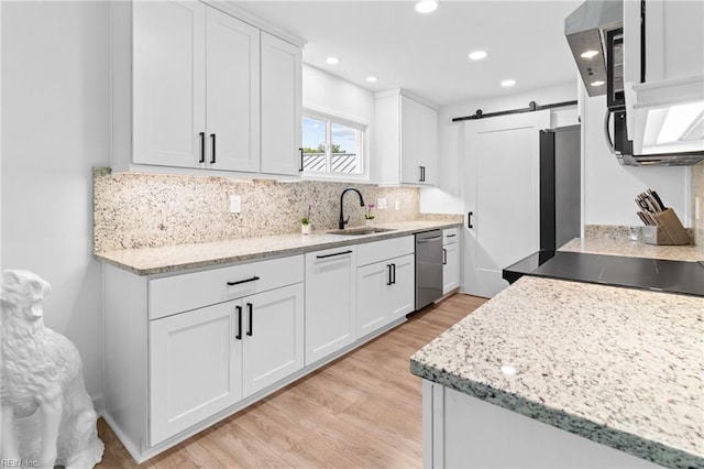 kitchen featuring a sink, stainless steel dishwasher, light wood finished floors, a barn door, and backsplash
