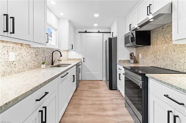 kitchen featuring stainless steel appliances, a barn door, a sink, under cabinet range hood, and white cabinetry