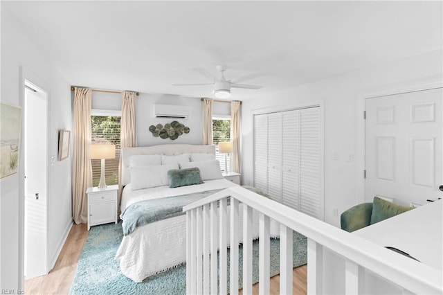 bedroom featuring an AC wall unit, multiple windows, and light wood-style floors