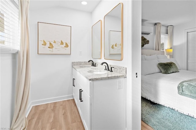 bathroom featuring ensuite bathroom, wood finished floors, a wall unit AC, double vanity, and baseboards