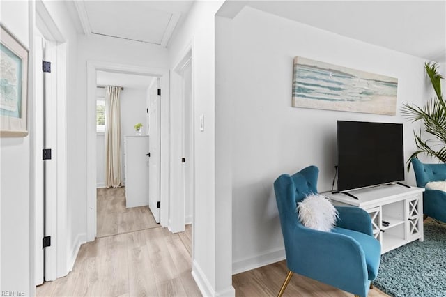 hallway with light wood-style floors, baseboards, and attic access