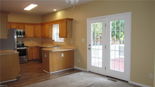 kitchen with stainless steel appliances, light countertops, a peninsula, a sink, and baseboards