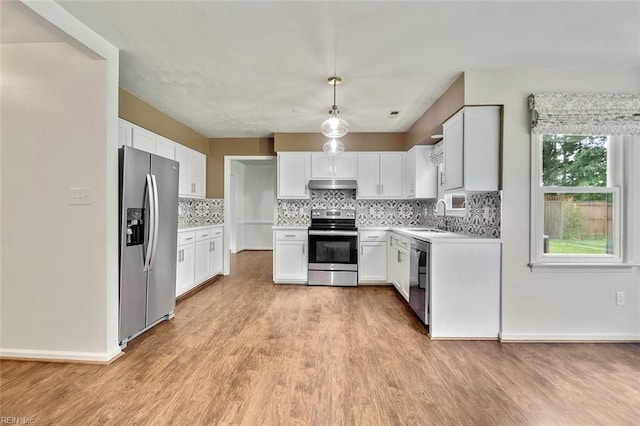kitchen featuring appliances with stainless steel finishes, under cabinet range hood, a sink, light wood-style flooring, and backsplash