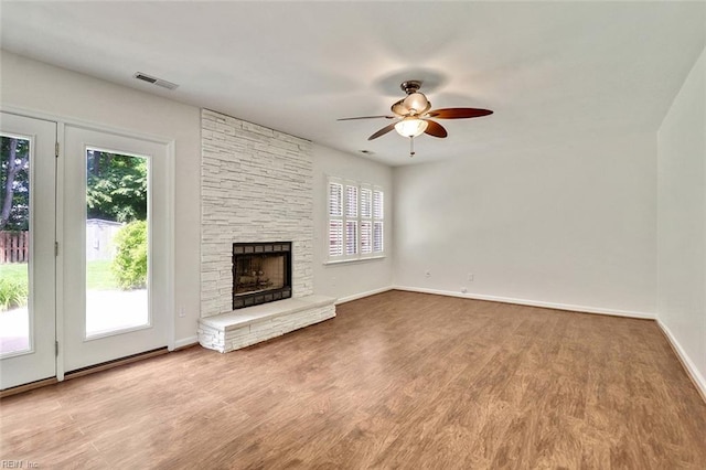 unfurnished living room featuring a ceiling fan, a stone fireplace, wood finished floors, and baseboards