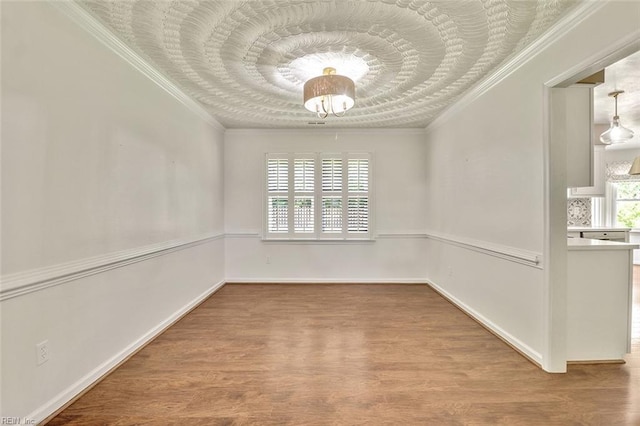 spare room featuring ornamental molding, wood finished floors, baseboards, and a chandelier