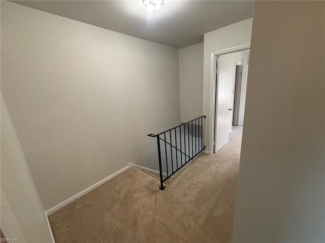 hallway featuring light colored carpet, an upstairs landing, and baseboards