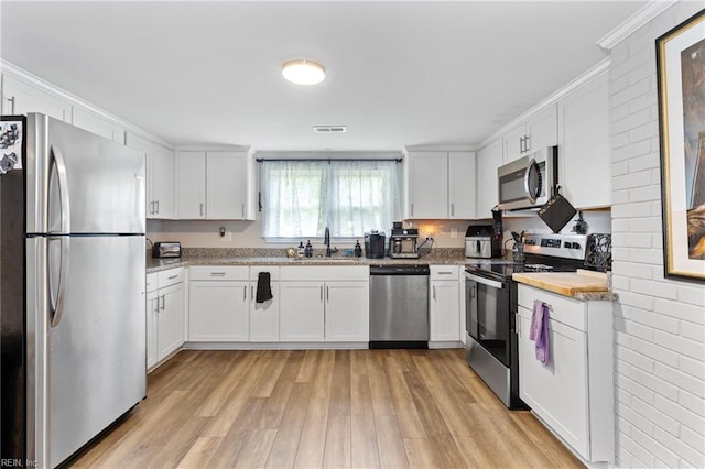 6944 Crittenden Rd, Suffolk, VA 23432 - kitchen with appliances with stainless steel finishes, a sink, light wood-type flooring, white cabinets, and ornamental molding