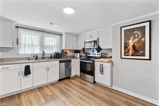 6944 Crittenden Rd, Suffolk, VA 23432 - kitchen with stainless steel appliances, a sink, brick wall, light wood finished floors, and white cabinetry