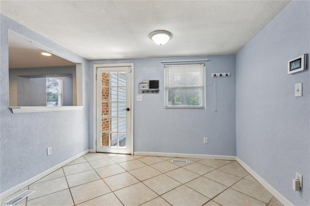 empty room with baseboards, tile patterned flooring, a textured ceiling, and a textured wall