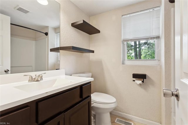 bathroom featuring toilet, vanity, baseboards, a textured wall, and a shower