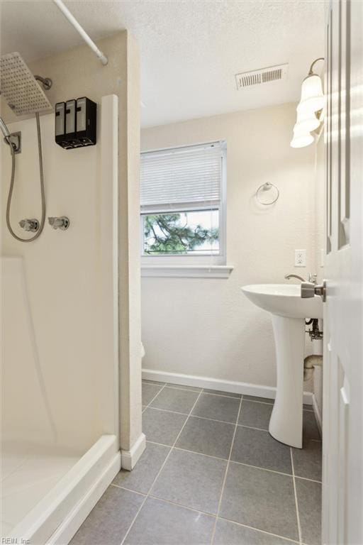 full bathroom with a stall shower, tile patterned floors, baseboards, and a sink