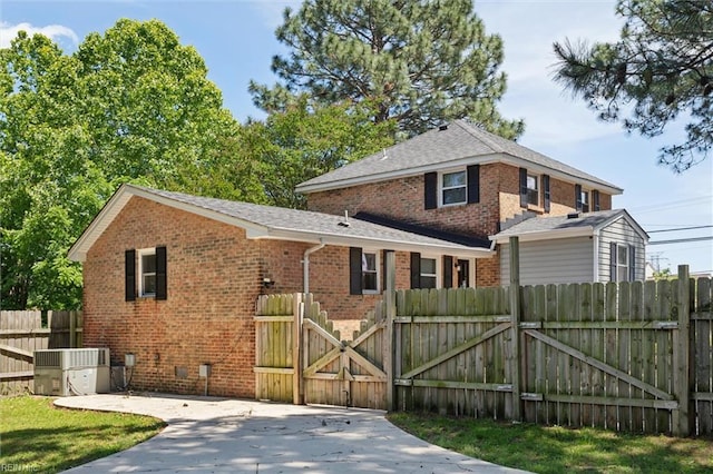 view of front of house featuring brick siding, a gate, cooling unit, and roof with shingles