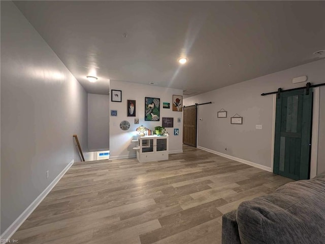 living room with a barn door, light wood-style flooring, and baseboards