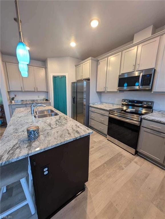 kitchen featuring stainless steel appliances, a sink, light stone countertops, a kitchen island with sink, and light wood-style flooring