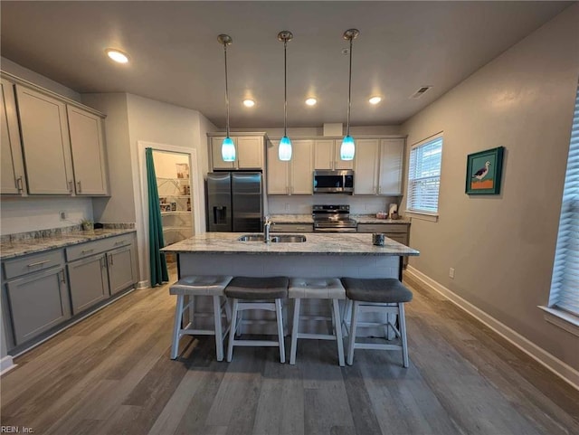 kitchen with stainless steel appliances, gray cabinets, a kitchen bar, baseboards, and dark wood-type flooring