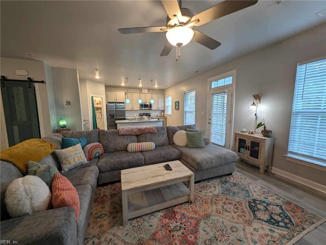 living area with a barn door, light wood-type flooring, a ceiling fan, and baseboards