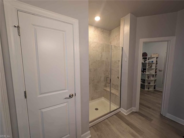 full bath featuring a stall shower, wood finished floors, baseboards, and a spacious closet