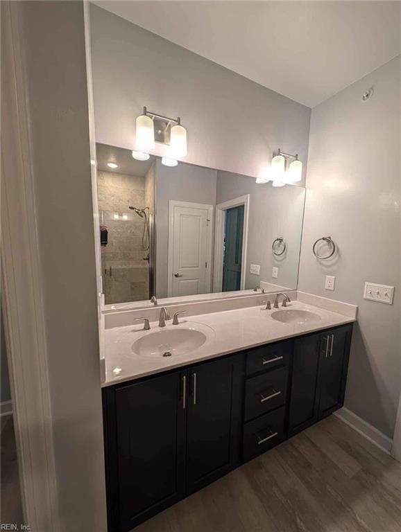 full bathroom with a shower stall, wood finished floors, double vanity, and baseboards