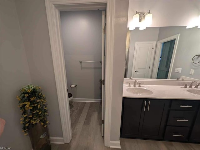 bathroom featuring wood finished floors, double vanity, toilet, and baseboards