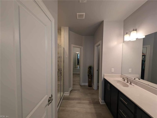bathroom with wood finished floors, a shower stall, baseboards, and vanity