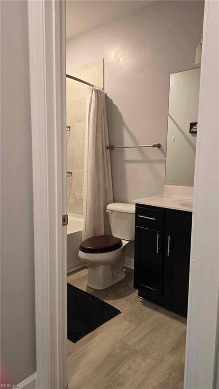 bathroom featuring toilet, vanity, wood finished floors, shower / bath combo, and baseboards