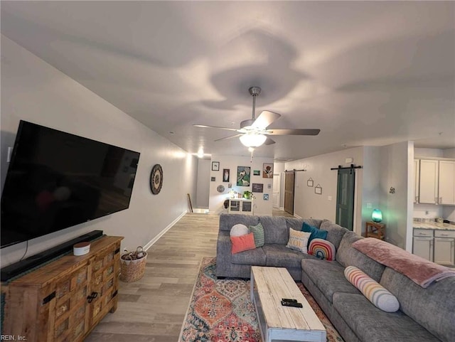 living area with a barn door, ceiling fan, light wood finished floors, and baseboards