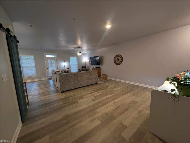 living area featuring light wood-style flooring, a barn door, baseboards, and ceiling fan
