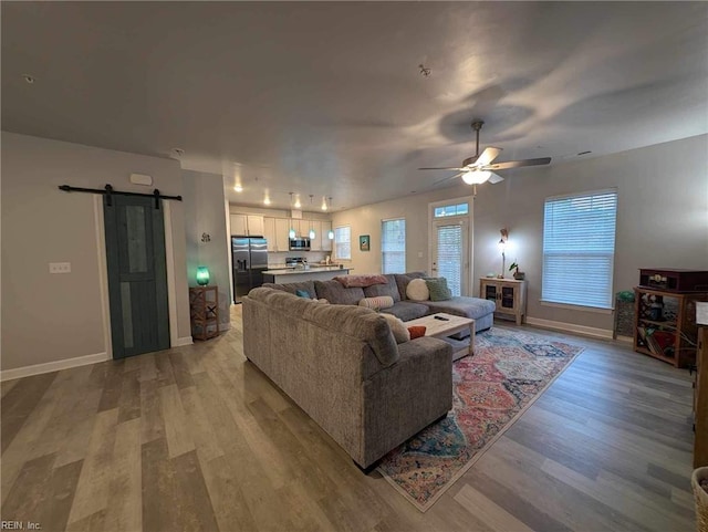 living room with a barn door, light wood finished floors, ceiling fan, and baseboards