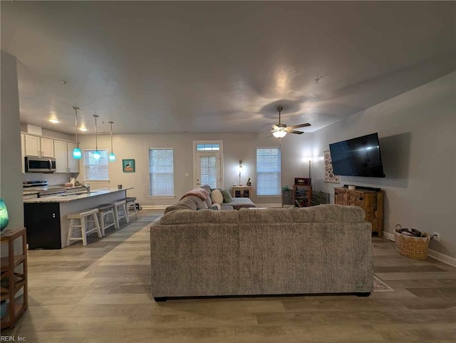 living room with baseboards, light wood-type flooring, and ceiling fan