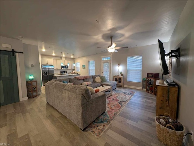 living room with a barn door, light wood finished floors, a ceiling fan, and baseboards