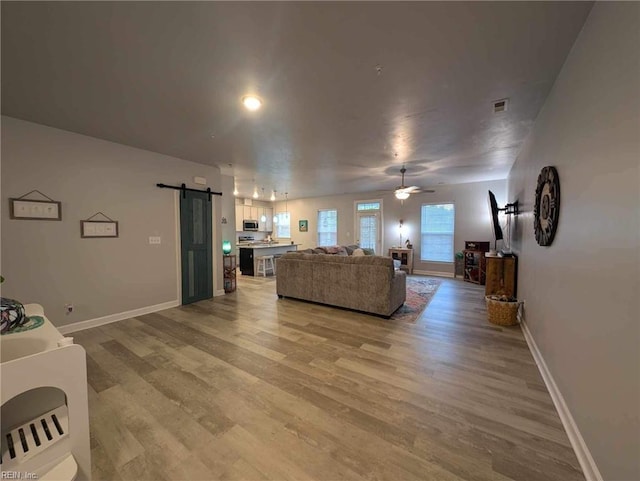 living room with a barn door, light wood-style floors, baseboards, and a ceiling fan