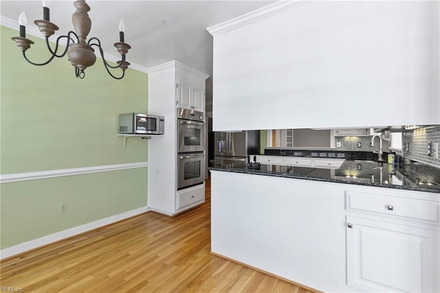 kitchen with appliances with stainless steel finishes, light wood-style flooring, a chandelier, ornamental molding, and white cabinetry