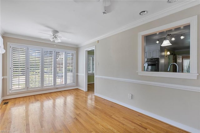 spare room featuring a ceiling fan, baseboards, crown molding, wood finished floors, and a sink