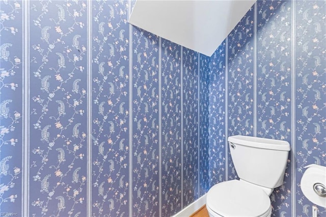 bathroom featuring toilet, wallpapered walls, baseboards, and wood finished floors